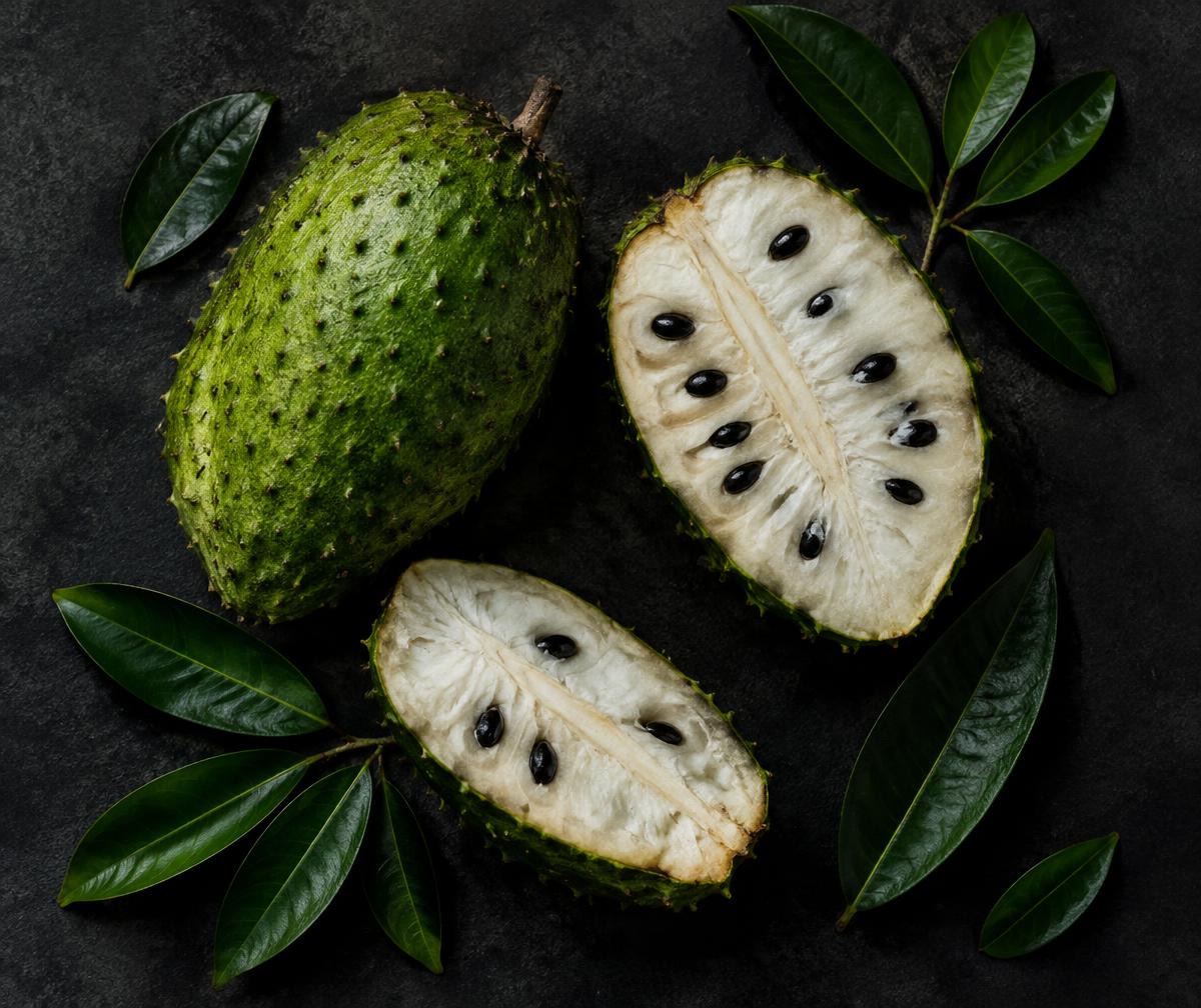 Fresh soursop fruit sliced open with leaves on a dark surface